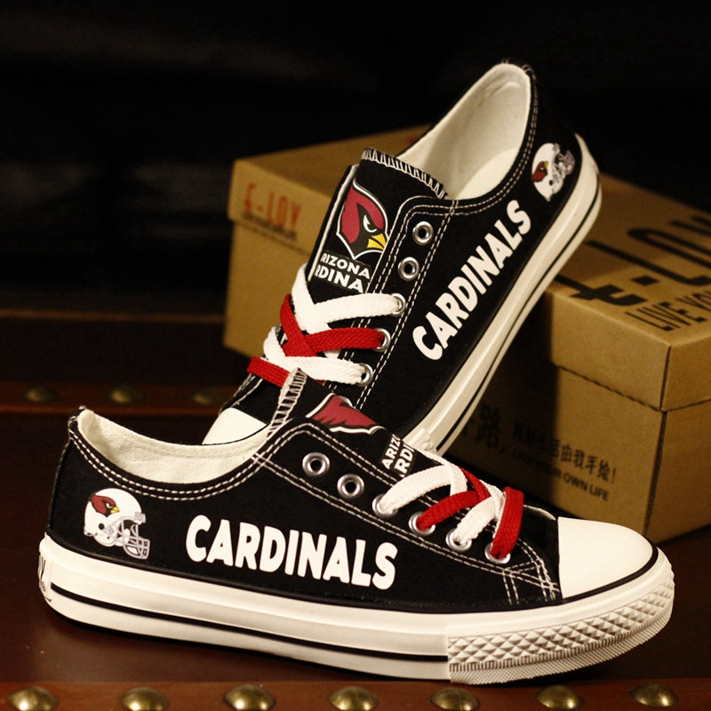 Black Cardinals canvas sneakers set against a dark background with shipping boxes. The shoes feature the Cardinals logo and helmet on the side.