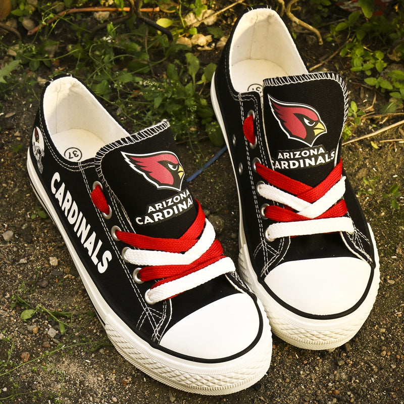 Pair of black Arizona Cardinals canvas low-top shoes on a dirt ground. Features red and white laces and the Cardinals logo and "CARDINALS" text.