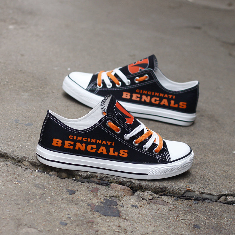 Black Cincinnati Bengals canvas sneakers resting on a concrete surface against a dark wall. Highlights the orange 'BENGALS' lettering and the B logo on the tongue.