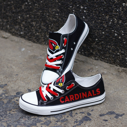 Black Arizona Cardinals canvas sneakers resting against a dark textured wall outdoors. Highlights the red 'CARDINALS' lettering and the cardinal head logo for an urban fan vibe.