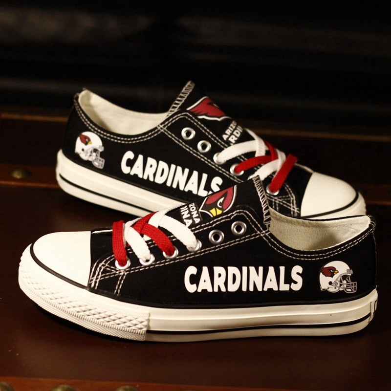 Black Arizona Cardinals canvas low-top shoes placed on a dark wooden surface. A clean shot showing the Cardinals logos and red laces.