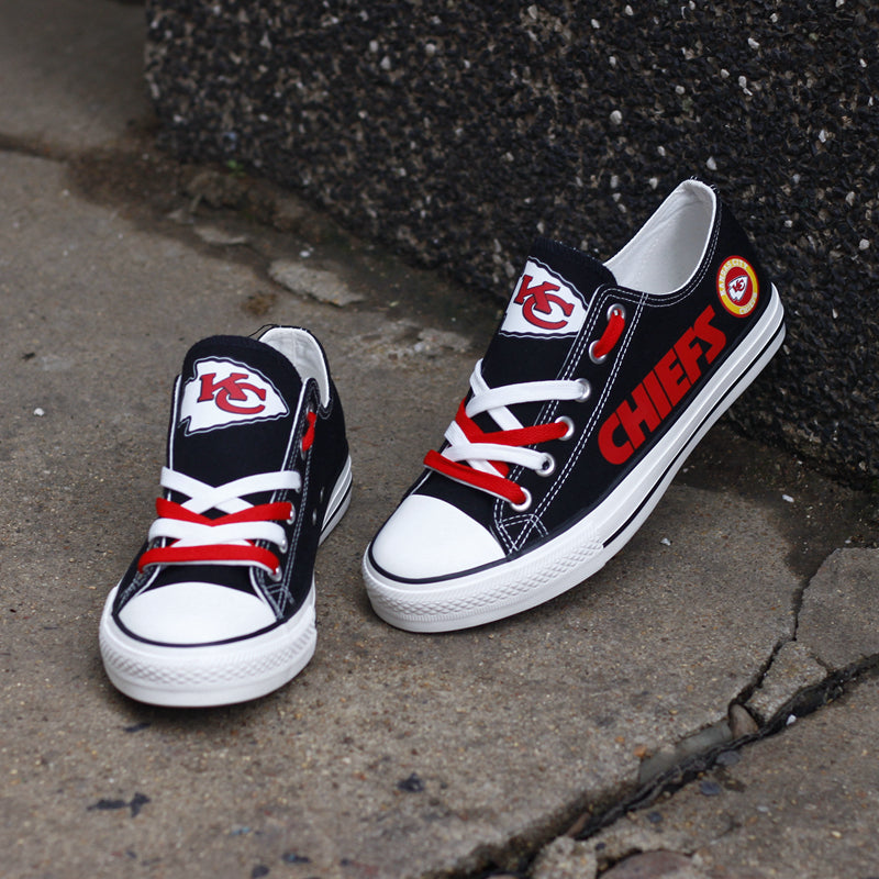 One large and one small black Kansas City Chiefs canvas sneaker leaning against a stone wall outdoors. Highlights the red 'CHIEFS' lettering and KC logo.