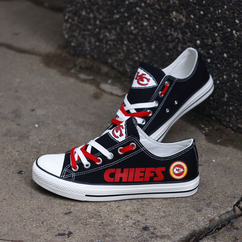 Pair of black Kansas City Chiefs canvas low-top shoes resting on concrete. Showcases the team logo on the tongue and the red laces for a dynamic look.