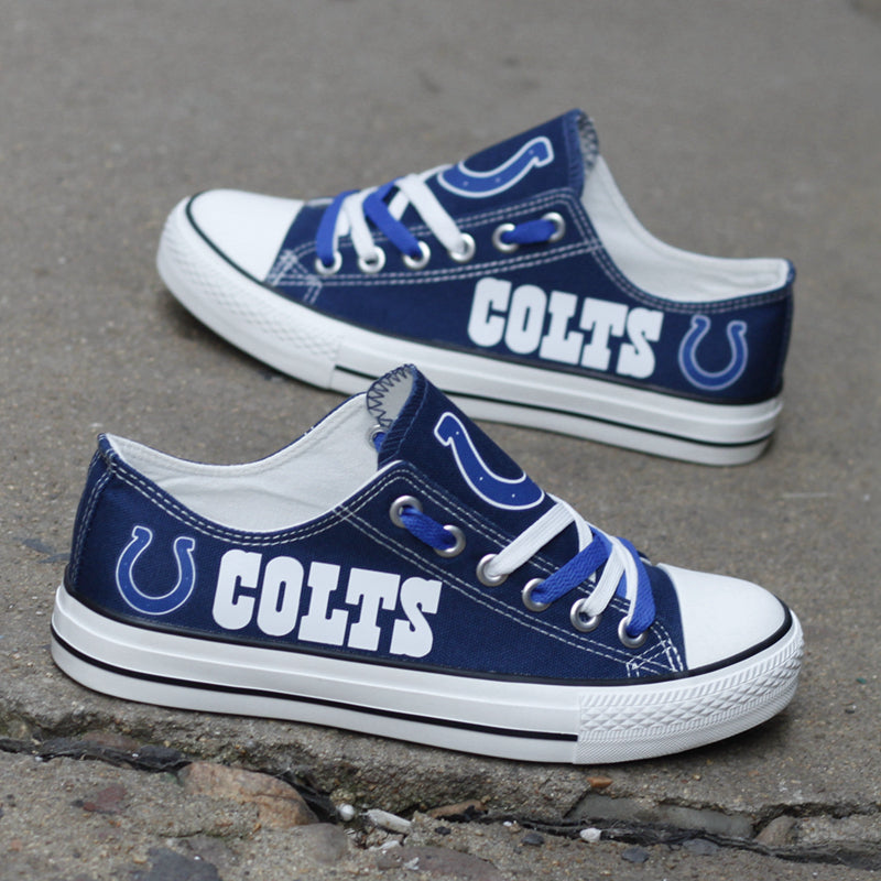Two blue Indianapolis Colts canvas low-top sneakers with white and blue laces, placed on a textured concrete ground. Shows team colors and logo.