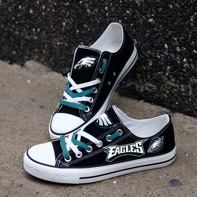 Black Philadelphia Eagles canvas sneakers resting against a dark textured wall outdoors. Highlights the white 'EAGLES' lettering and green accents for an urban fan vibe.