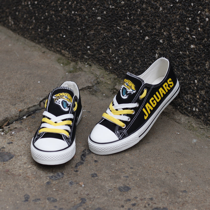 One large and one small black Jacksonville Jaguars canvas sneaker leaning against a stone wall outdoors. Shows the yellow laces and the iconic jaguar head logo.