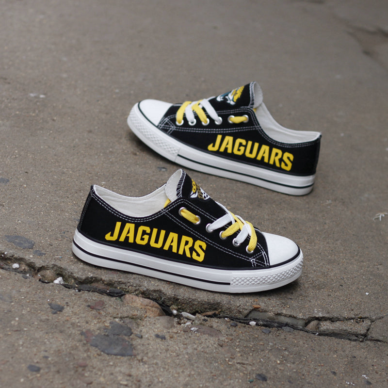 Pair of black Jacksonville Jaguars canvas low-top shoes on a gray concrete surface. Features the vibrant yellow 'JAGUARS' lettering and the classic team emblem.