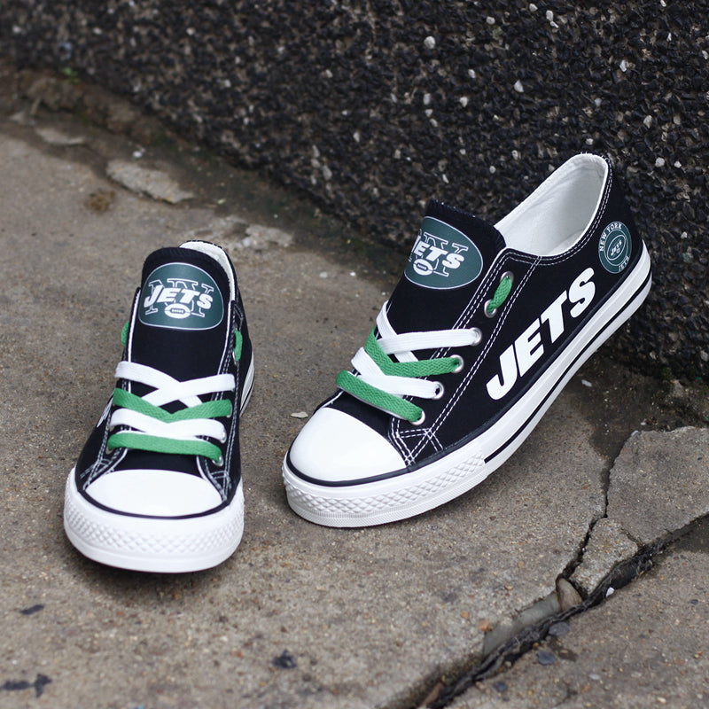 One large and one small black New York Jets canvas sneaker resting on concrete against a dark wall. Highlights the white 'JETS' lettering and green laces.