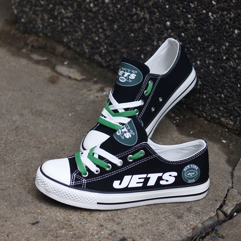 One black New York Jets canvas shoe leaning against a dark wall, angled upward. Focuses on the white 'JETS' text and the circular team logo.