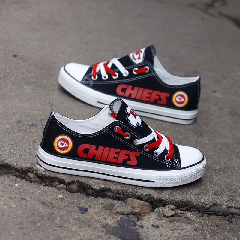Pair of black Kansas City Chiefs canvas sneakers sitting on a concrete surface, angled upward. Focuses on the bold red 'CHIEFS' text and team logo patch.