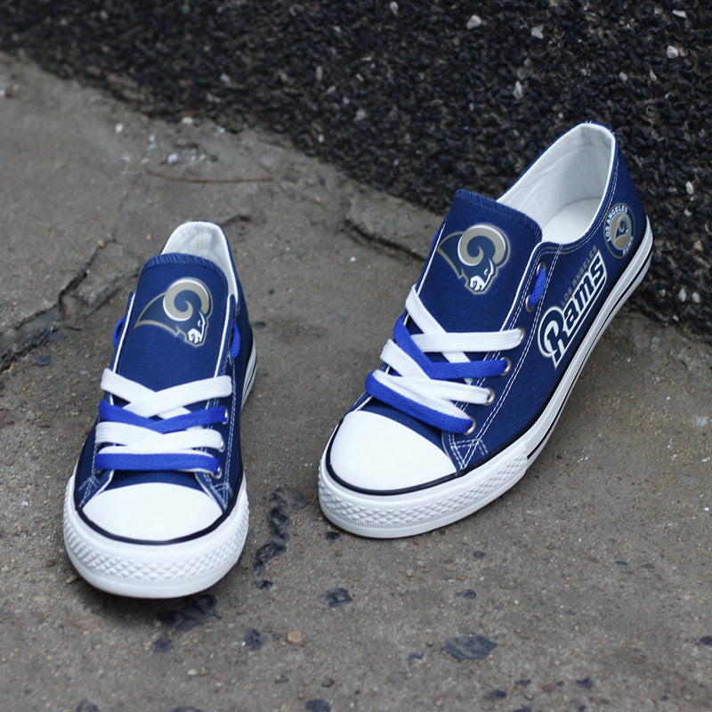 One royal blue Los Angeles Rams canvas shoe leaning against a dark wall, angled upward. Focuses on the gold 'RAMS' text and the classic team logo emblem.