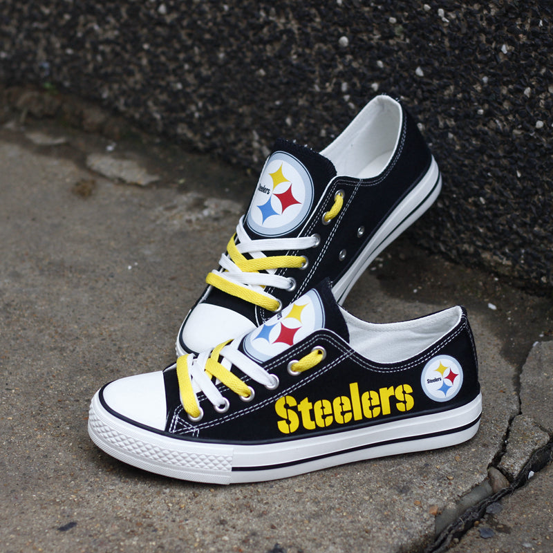 One black Pittsburgh Steelers canvas shoe leaning against a dark wall, angled upward. Focuses on the yellow 'Steelers' text and the classic team emblem.