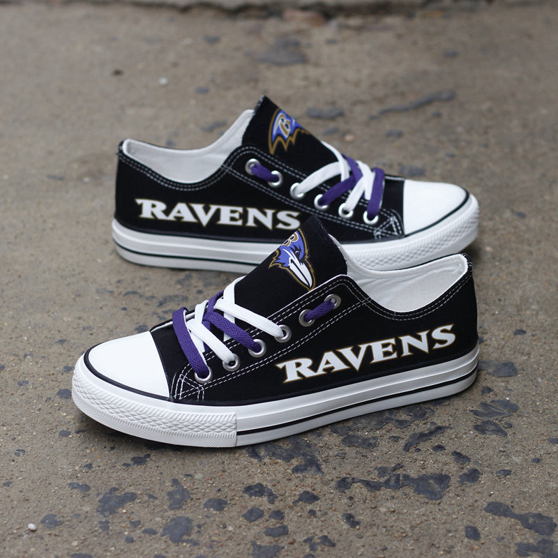 Black Baltimore Ravens canvas sneakers leaning against a dark textured wall outdoors. Highlights the bold 'RAVENS' lettering and purple and white laces for a rugged look.