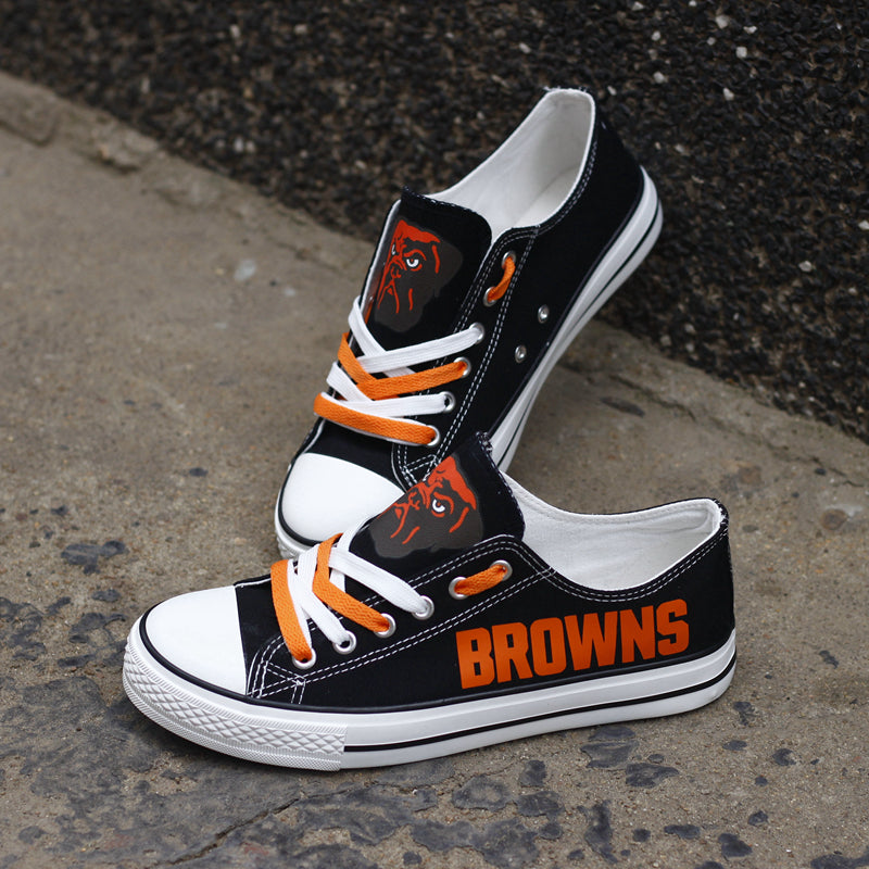 Black Cleveland Browns canvas sneakers resting against a dark textured wall outdoors. Highlights the orange 'BROWNS' lettering and the team logo for an urban fan vibe.