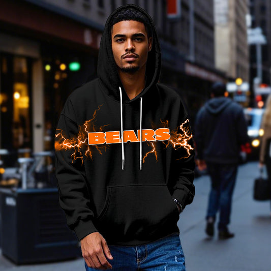 Male model wearing a black Chicago Bears pullover hoodie with bright orange lightning graphics, standing in a city street. The Bears apparel is shown being worn casually.