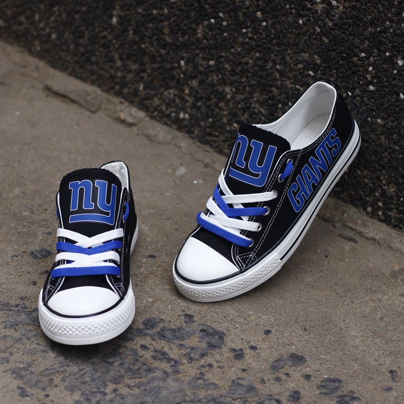 Black New York Giants canvas sneakers resting against a dark textured wall outdoors. Highlights the blue 'GIANTS' lettering and the 'NY' logo for an urban fan vibe.