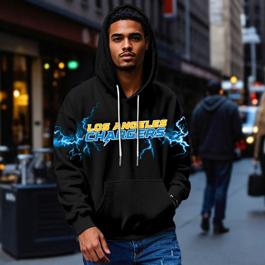Male model wearing a black Los Angeles Chargers pullover hoodie with bright blue lightning graphics, standing in a city street. The Chargers apparel is shown being worn casually.