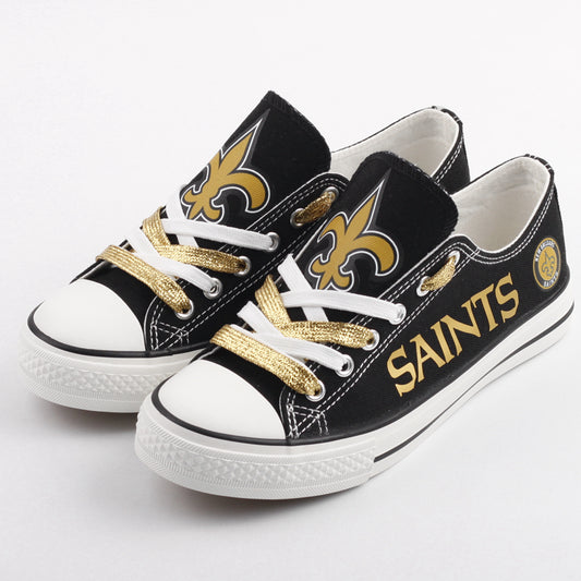 Pair of black New Orleans Saints canvas shoes with gold glitter and white laces. Features the large gold fleur-de-lis logo.