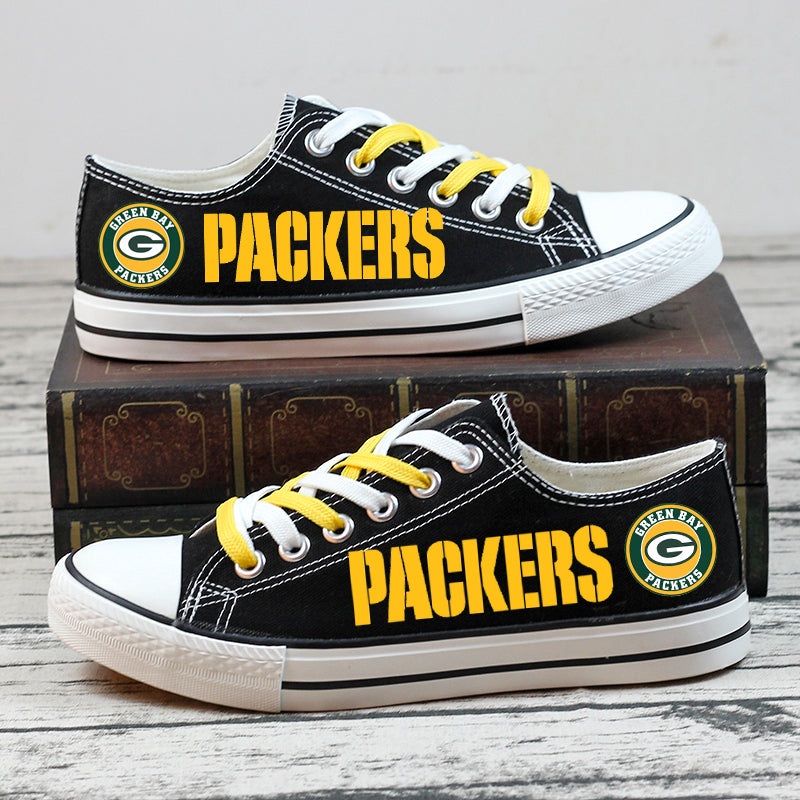 Stacked pair of black Green Bay Packers low-top canvas sneakers with yellow PACKERS text and team logo, photographed on a stack of books.