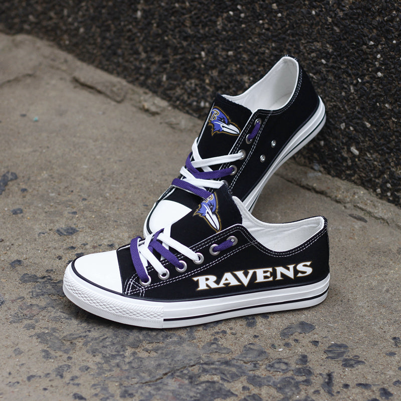 Black Baltimore Ravens canvas sneakers leaning against a dark textured wall outdoors. Highlights the bold 'RAVENS' lettering and purple and white laces for a rugged look.