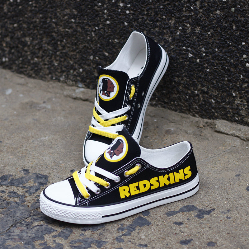 Black Washington Redskins canvas sneakers resting against a dark textured wall outdoors. Highlights the yellow 'REDSKINS' lettering and the team logo for an urban fan vibe.