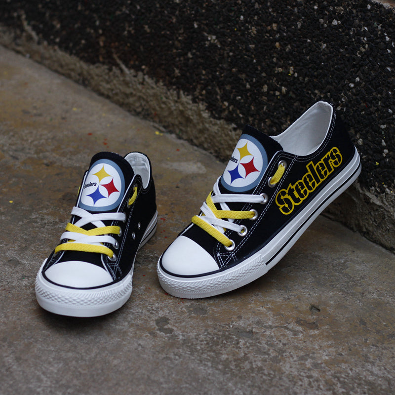 One large and one small black Pittsburgh Steelers canvas sneaker on a concrete surface. Shows the yellow laces and the iconic three-star Steelers logo.