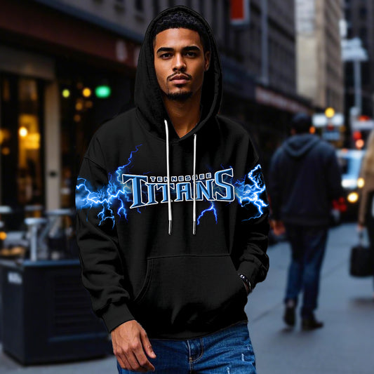 Male model wearing a black Tennessee Titans pullover hoodie with bright blue lightning graphics, standing in a city street. The Titans apparel is shown being worn casually.