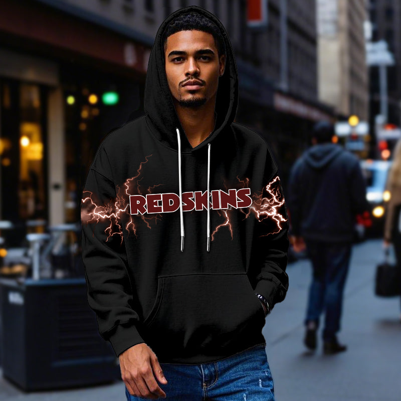 Male model wearing a black Washington Redskins pullover hoodie with bright maroon lightning graphics, standing in a city street. The Redskins apparel is shown being worn casually.
