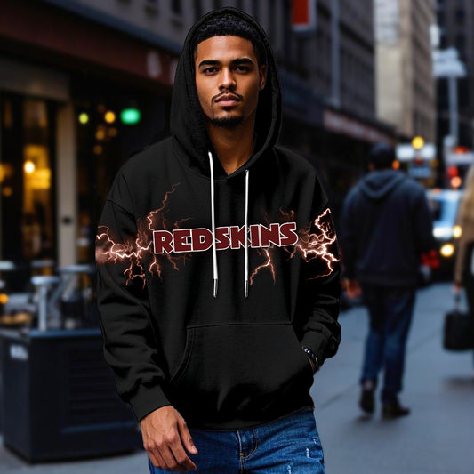Male model wearing a black Washington Redskins pullover hoodie with bright maroon lightning graphics, standing in a city street. The Redskins apparel is shown being worn casually.