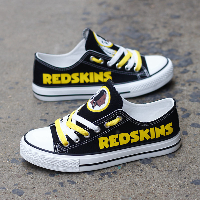 One large and one small black Washington Redskins canvas sneaker leaning against a dark textured wall outdoors. Shows the yellow laces and the iconic team logo.